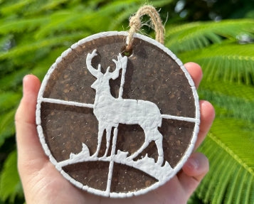 Decorative circular ornament with a deer silhouette held against a green leafy background