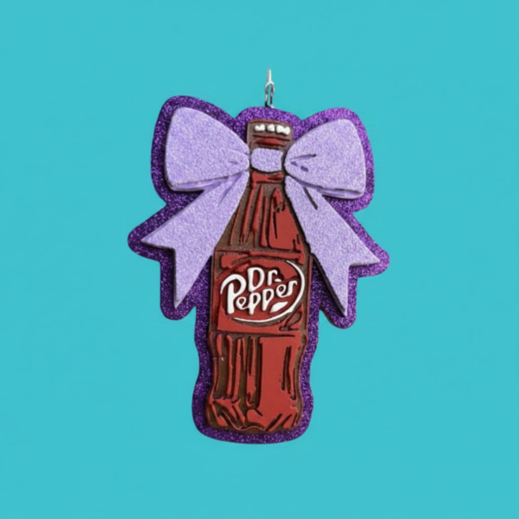 Dr Pepper bottle-shaped ornament with a large bow on a pink wooden background