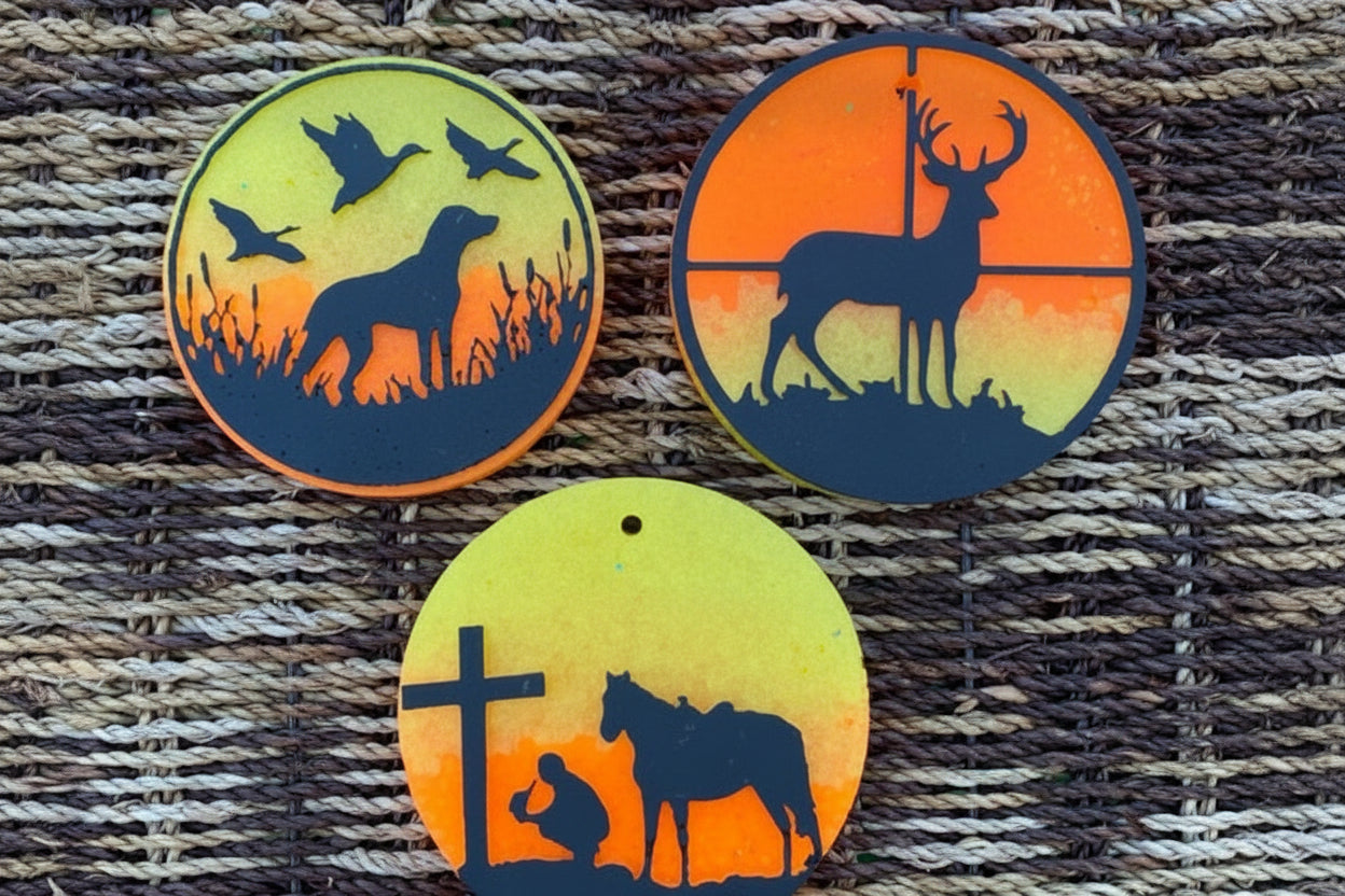 Three circular car fresheners with nature-themed designs on a woven surface.