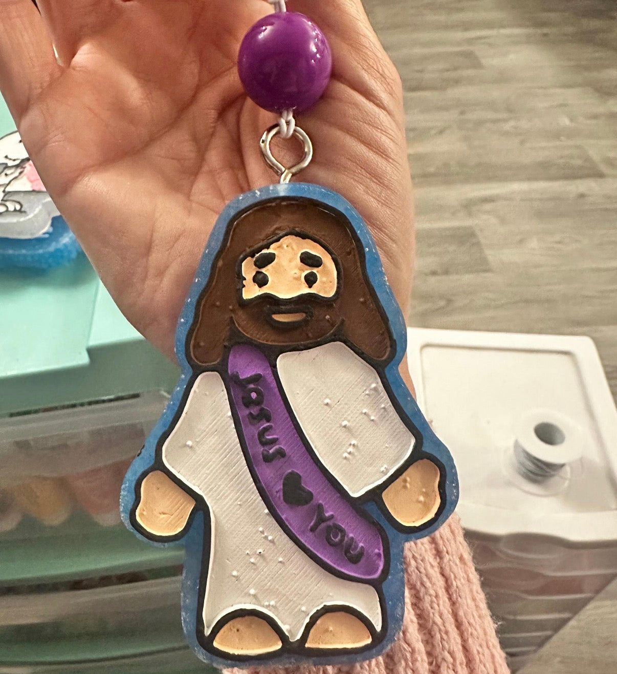 Keychain with a character wearing a purple scarf with 'I love you' text, held by a hand.