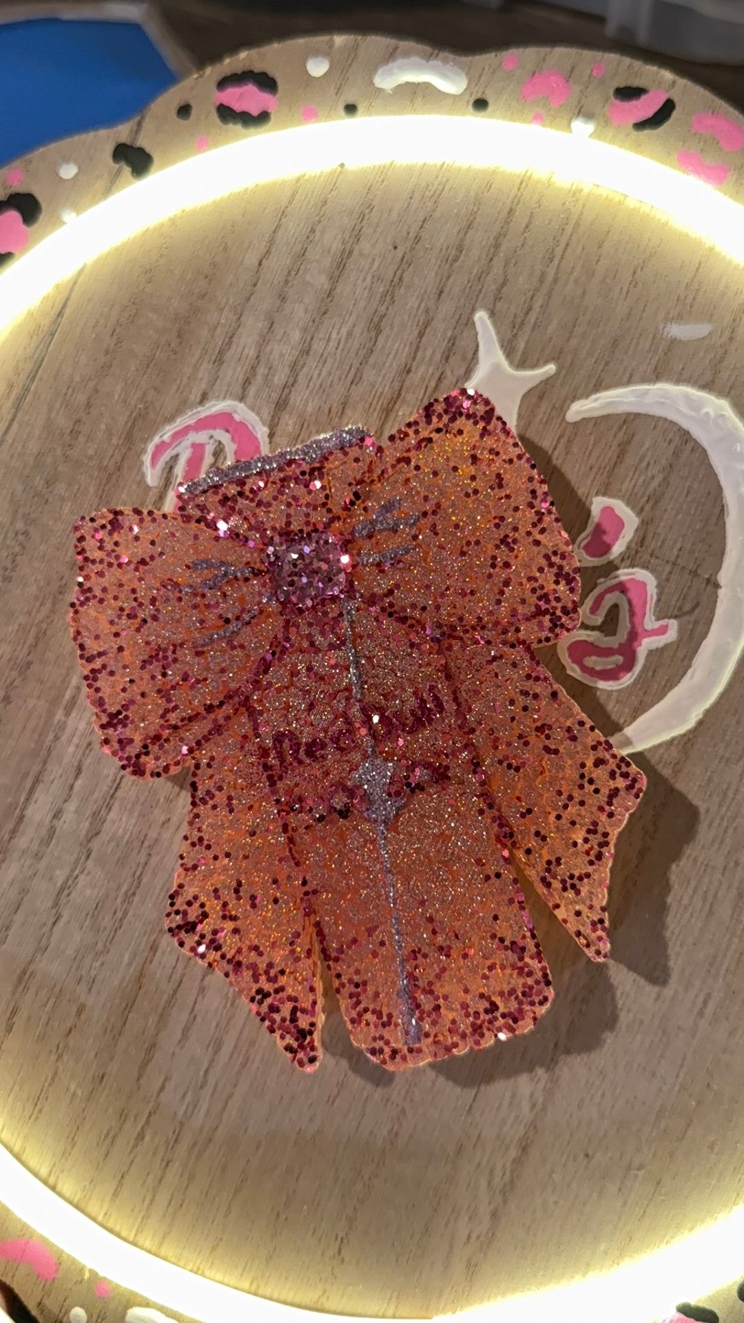 Decorative pink bow with glitter on a wooden hoop with floral patterns.