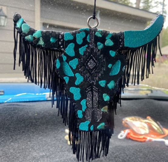 Decorative car hanging with teal and black pattern on a car dashboard.